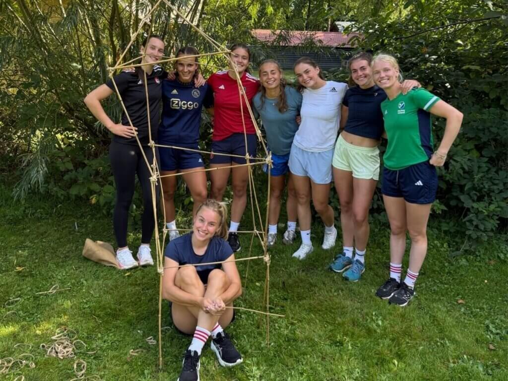 Een groep deelnemers bouwt samen een bamboeconstructie tijdens een teambuildingopdracht van Move For Fun.