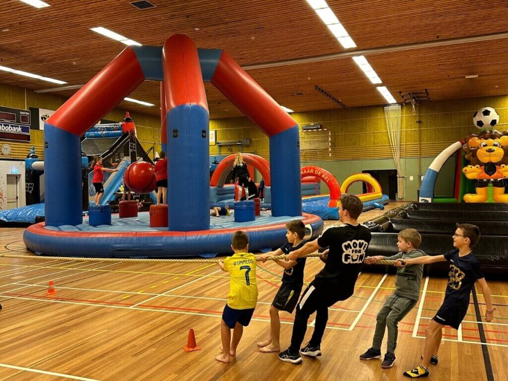Kinderen doen mee aan een touwtrekwedstrijd tijdens het Vakantie Fun evenement in sporthal De Pijl in Naaldwijk met opblaasbare attracties.