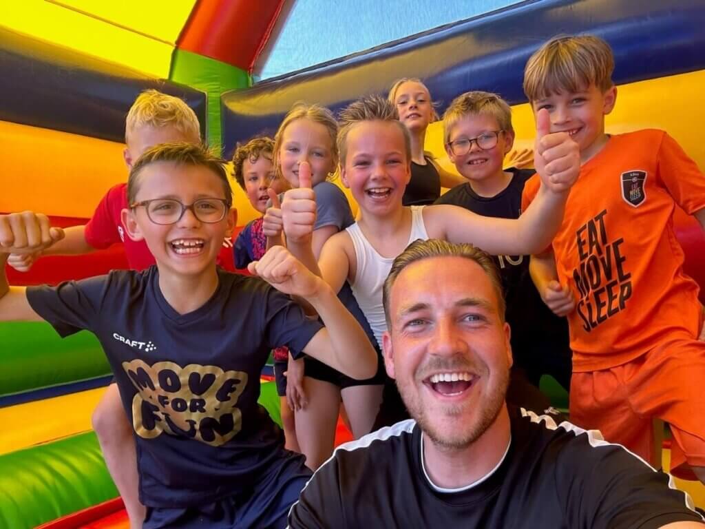 Kinderen lachen en geven een duim omhoog tijdens een vrolijk schoolreisje van Move For Fun in een kleurrijk springkussen.