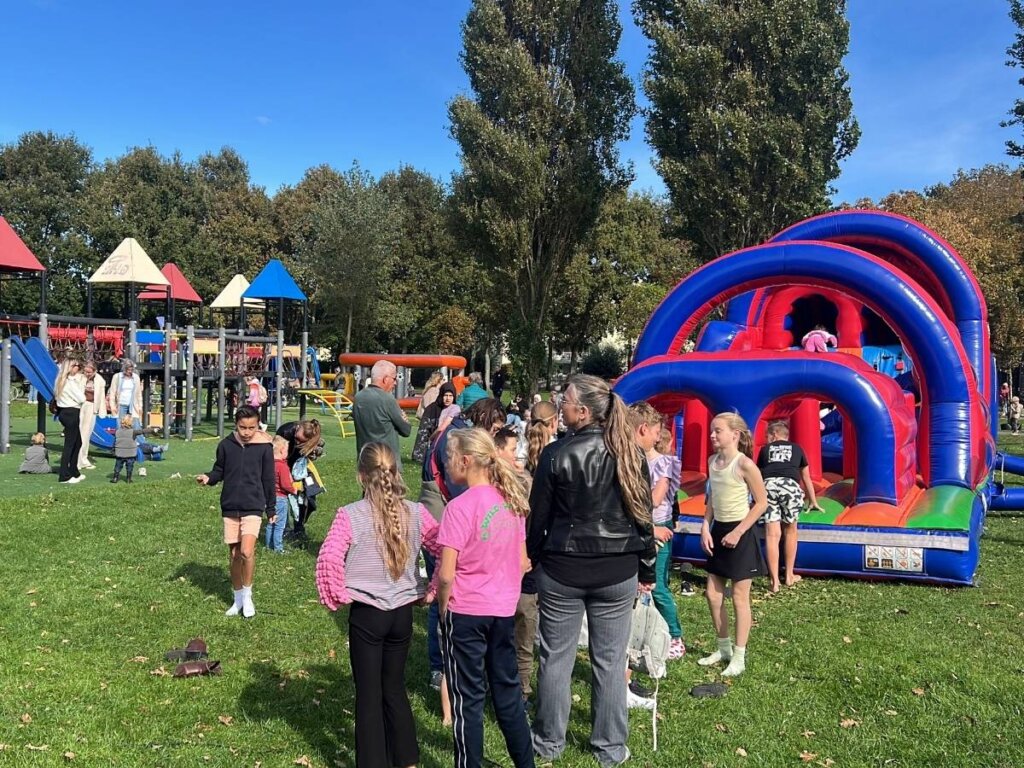 Kinderen staan in de rij en rennen over een opblaasbare stormbaan in een park in het Westland tijdens een buitenspeeldag van Move For Fun