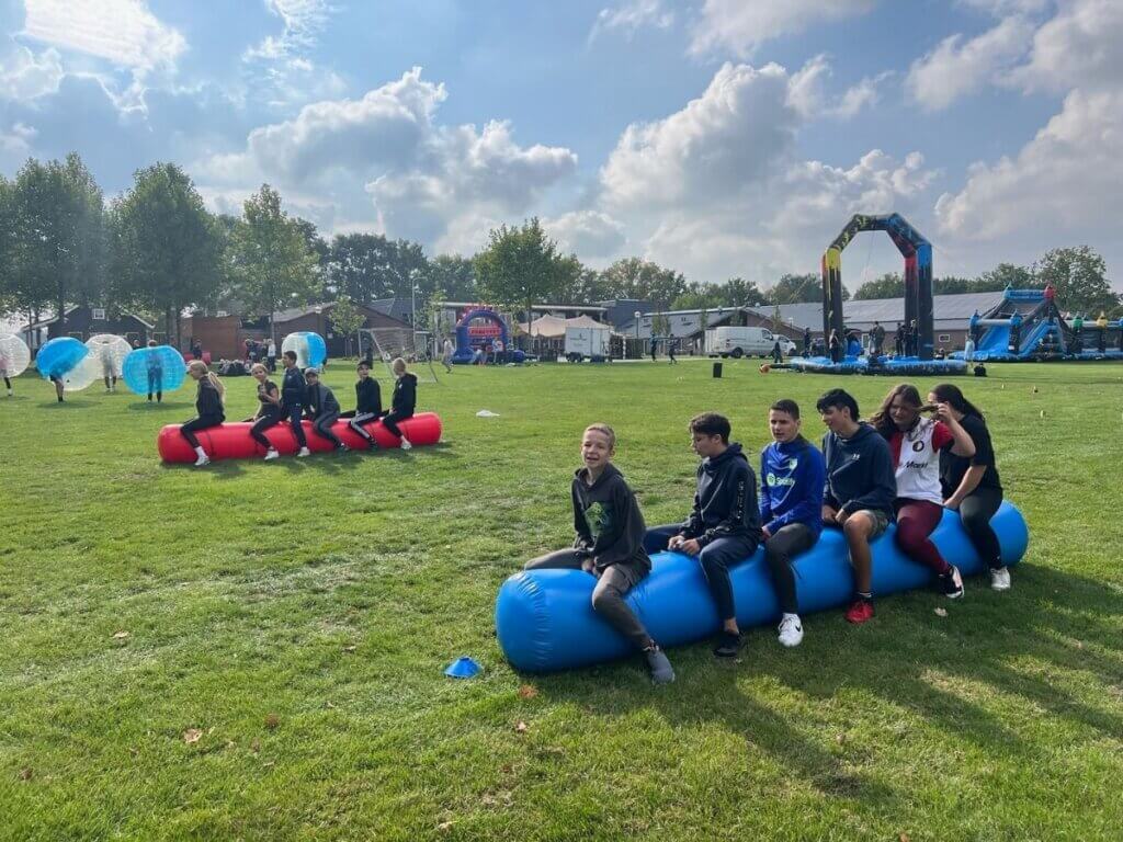 Twee teams nemen deel aan een balans- en racespel op opblaasbare zitbuizen tijdens een introductiedag van Move For Fun.