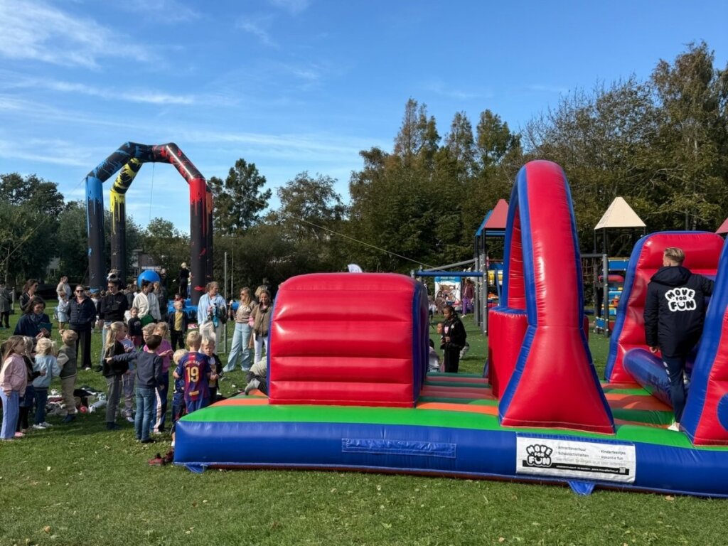 Kinderen doen mee aan een springkussen parcours tijdens een buitenspeeldag van Move For Fun