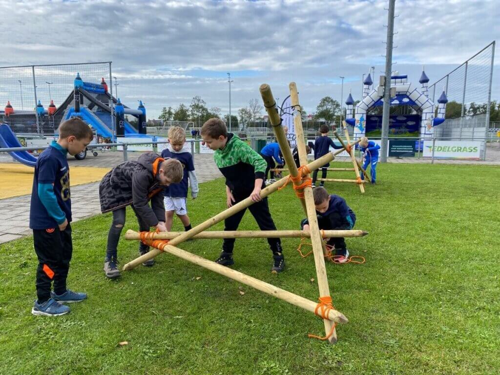 Een groep kinderen werkt samen om een katapult te bouwen tijdens een teambuildingactiviteit van Move For Fun, waarbij samenwerking en techniek centraal staan.