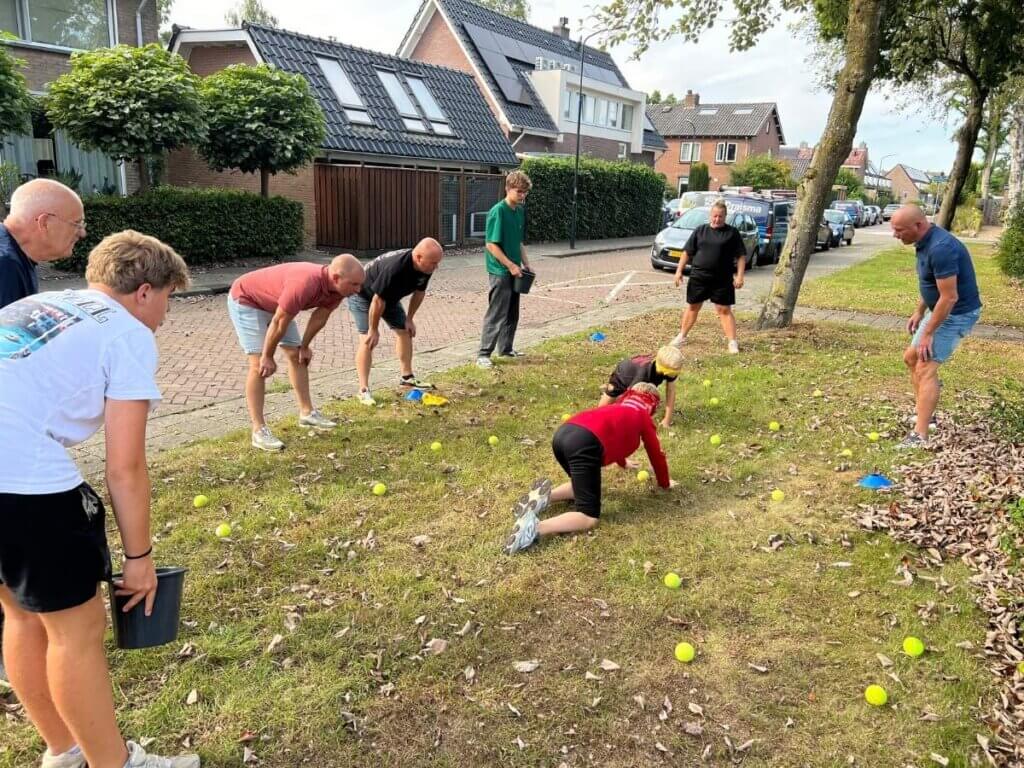 Volwassenen en kinderen spelen een actief spel met tennisballen tijdens Burendag in de wijk.