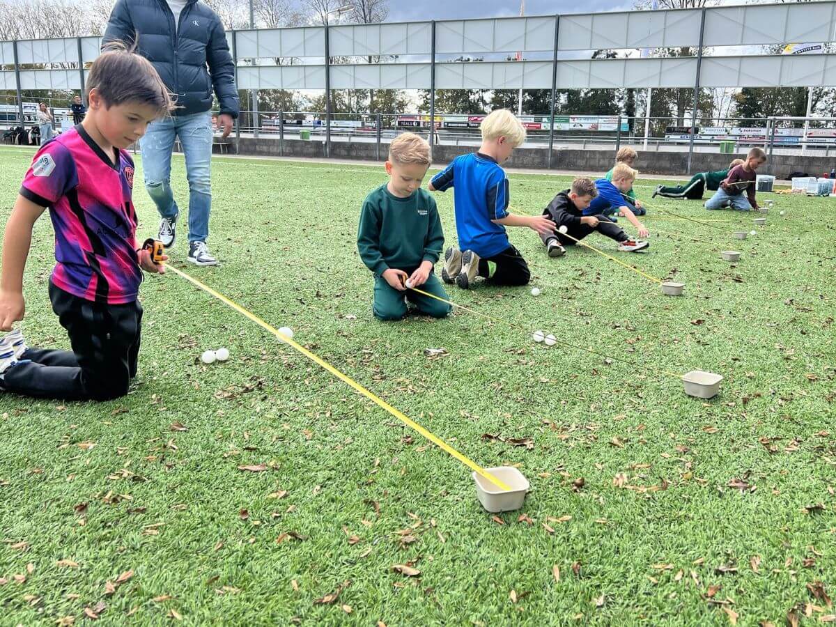 alleskunner-kinderfeestje-westland-meetspel-afstand-meten Kinderen rollen pingpongballen over een meetlint tijdens een Alleskunner opdracht buiten.