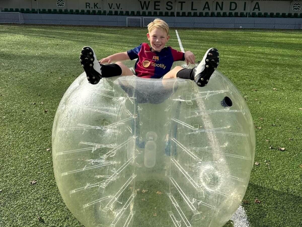 Kind speelt op bubbelbal tijdens Bubbelvoetbal feest Jongen zit bovenop bubbelbal tijdens Bubbel Voetbal kinderfeestje bij Westlandia.