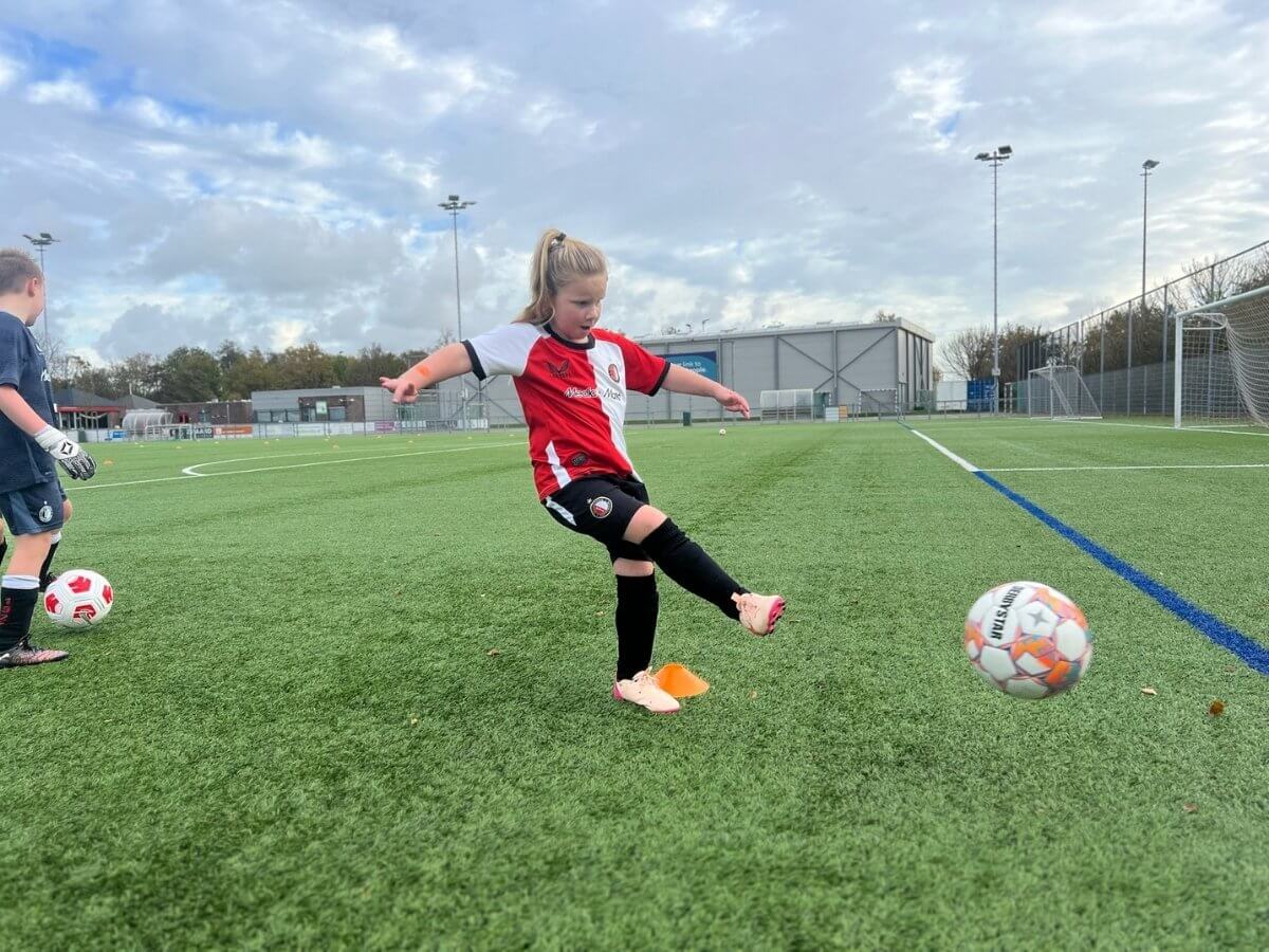 Voetbal schotoefening – Jong meisje trapt de bal richting doel Jongen trapt een voetbal tijdens een oefening op het veld bij het voetbal kinderfeestje van Move For Fun.