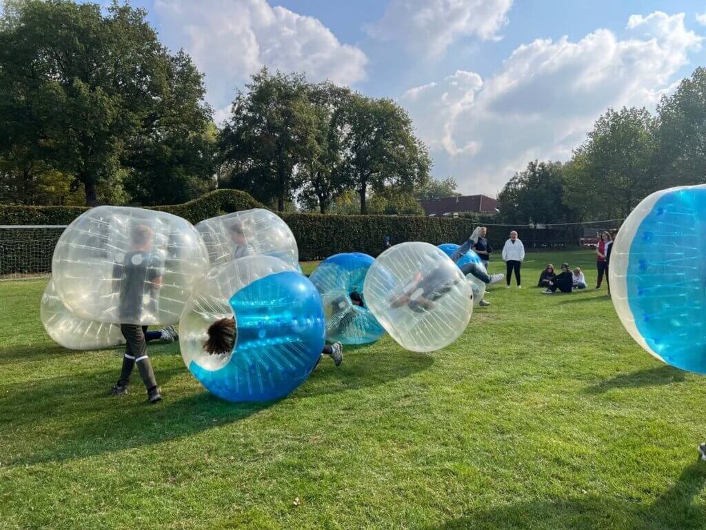 Deelnemers rennen en botsen in bubbelballen tijdens een bubbelvoetbal teamuitje van Move For Fun