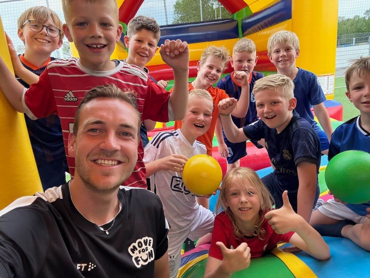 Kinderen tijdens Vakantie Fun op een springkussen van Move For Fun Kinderen lachen en poseren samen met een Move For Fun begeleider op een springkussen tijdens Vakantie Fun.