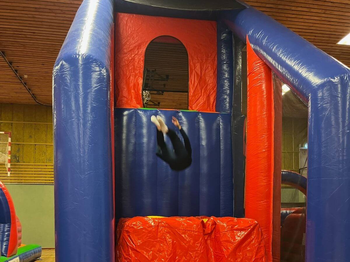 Actieve stormbaan tijdens sport- en speldag – Move For Fun Kind springt van een hoge stormbaan tijdens een sport- en speldag met springkussens in Sporthal De Pijl